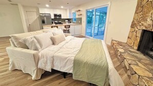 Une chambre moderne avec un grand lit, une cheminée en pierre et une vue sur la cuisine et l’espace extérieur.
