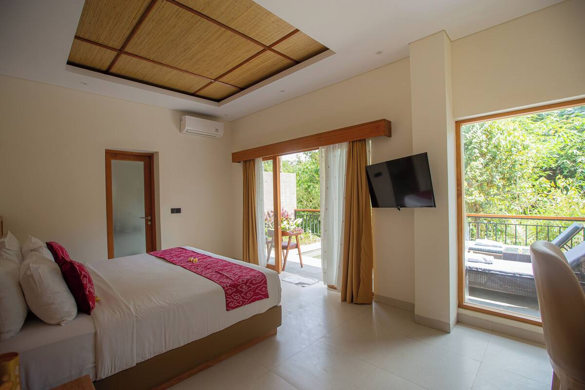 A bedroom with a bed, a TV, a balcony with a chair, and a door.