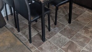Un comedor con una mesa de mármol, sillas negras, un florero con flores, una ventana con persianas, un microondas y armarios.