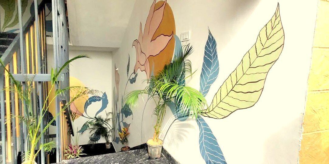 A staircase with a metal railing, a wall with a mural of a woman and leaves, and several potted plants.