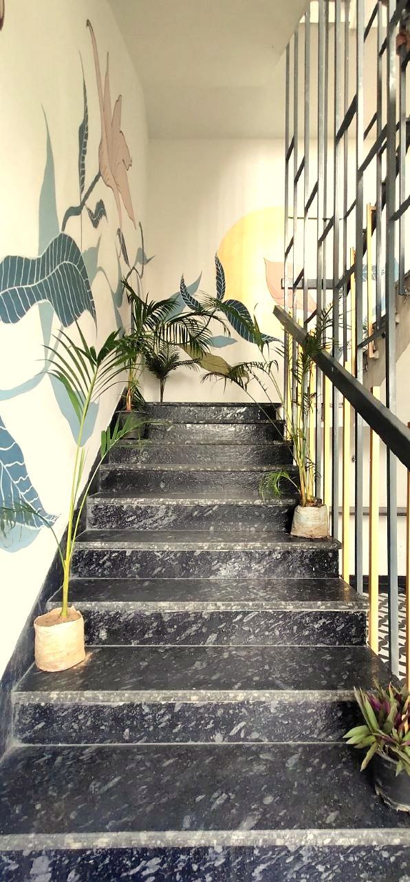 A staircase with black marble steps, flanked by potted plants and a mural of a dinosaur.