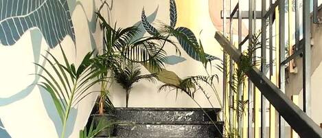 A staircase with black marble steps, flanked by potted plants and a mural of a dinosaur.