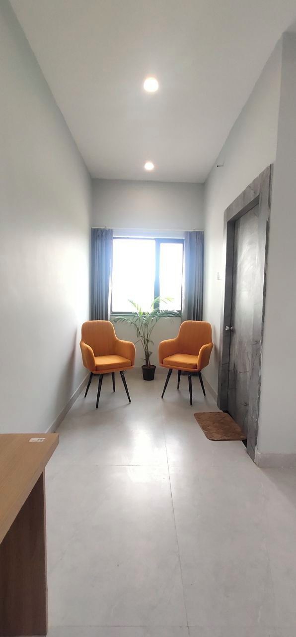 A room with two orange chairs, a potted plant, a wooden table, and a door with a textured surface.