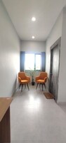 Una habitación con dos sillones naranja, una planta en maceta, una mesa de madera y una puerta con superficie texturizada.