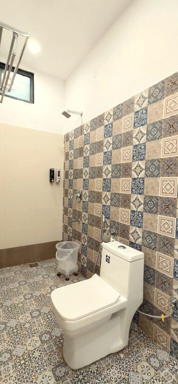 A bathroom with a toilet, a shower, and patterned tiles on the walls and floor. - Kunj - By Shivaneel Hospitality (Pushkar)