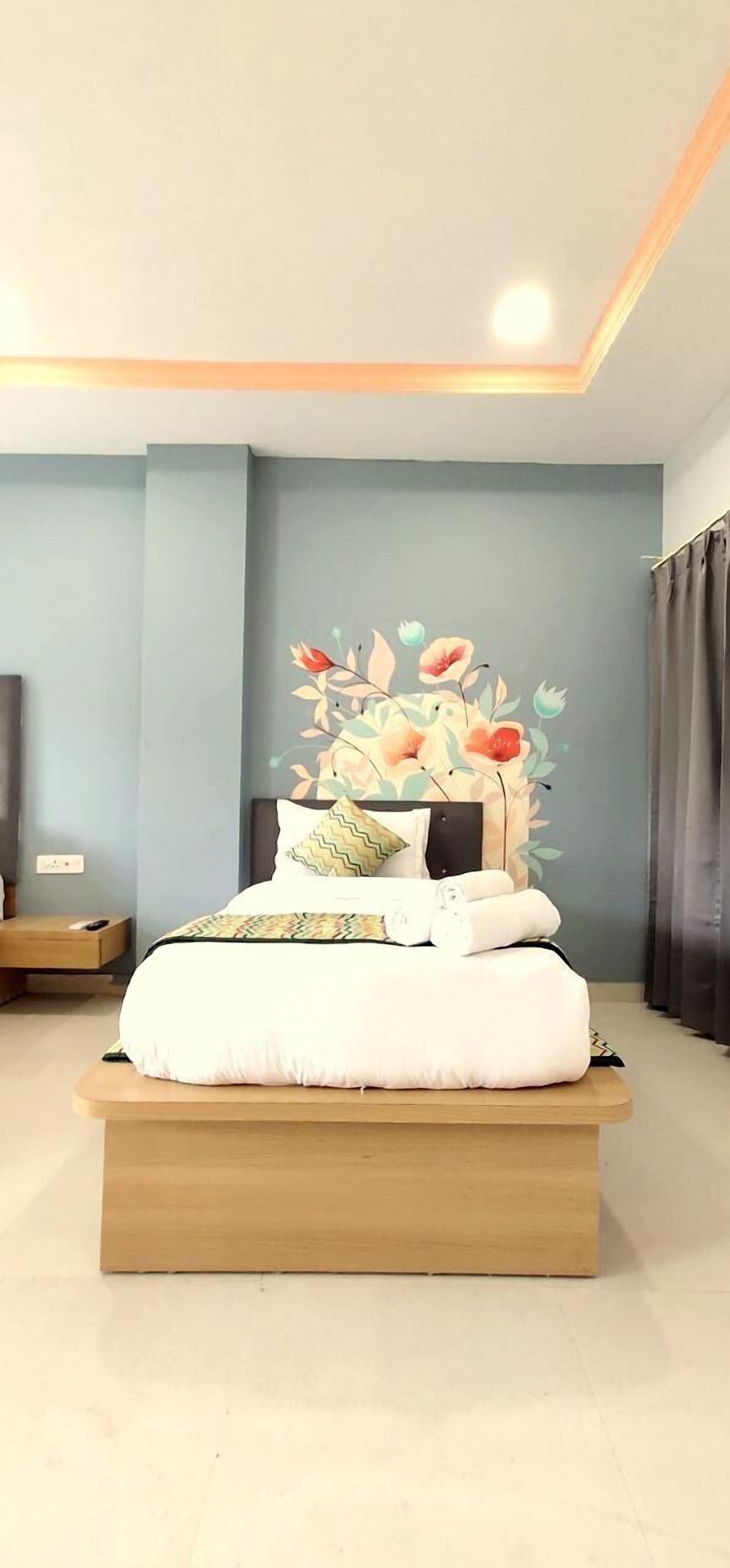 A modern bedroom with a bed centered on a platform, a decorative wall mural, and a nightstand with a lamp.