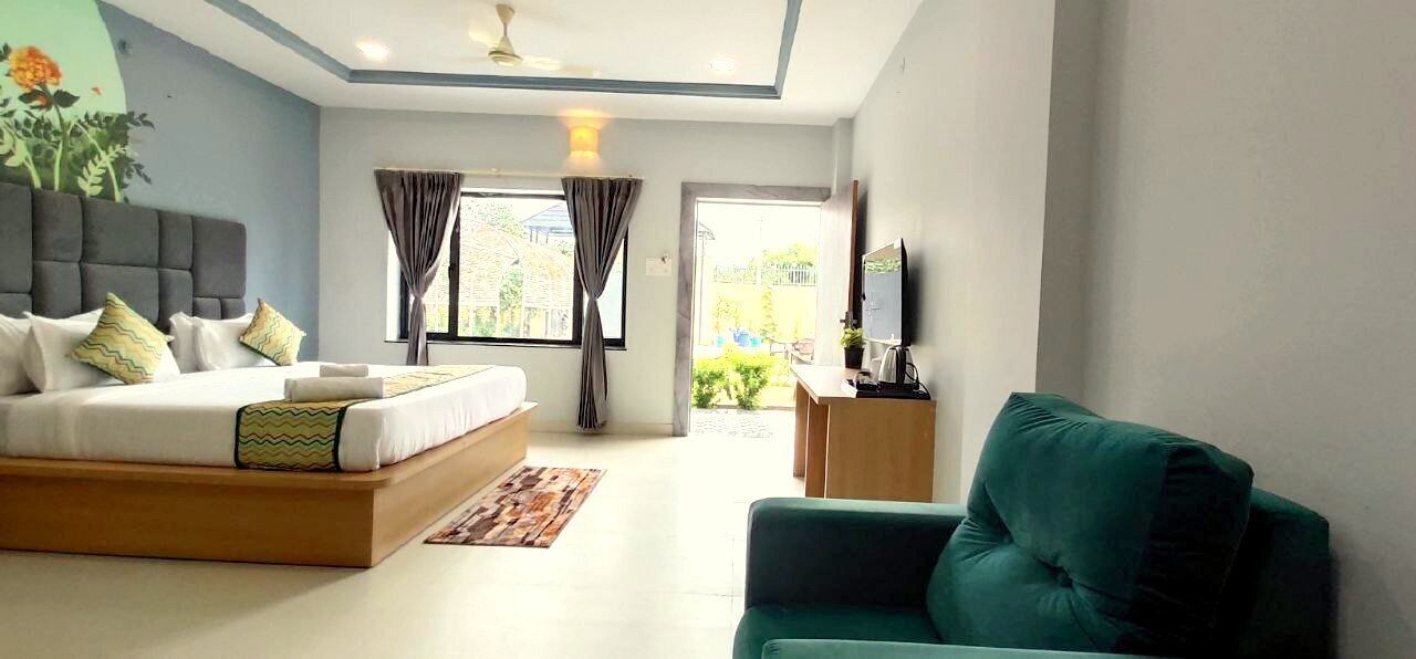 A modern bedroom with a large bed, a green armchair, a TV, and a ceiling fan.