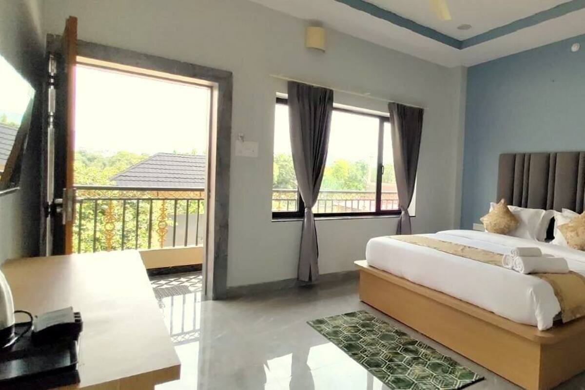 A hotel room with a bed, a desk, a chair, a window with curtains, and a balcony.