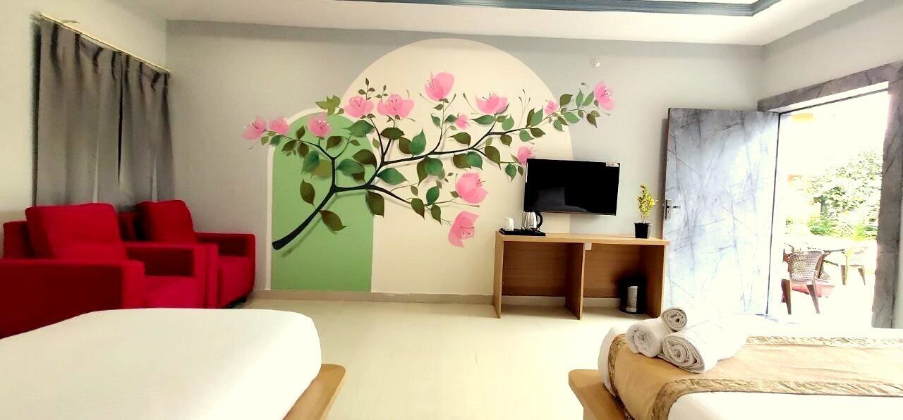 A hotel room with a bed, red chairs, a TV, a wooden desk, and a wall mural.