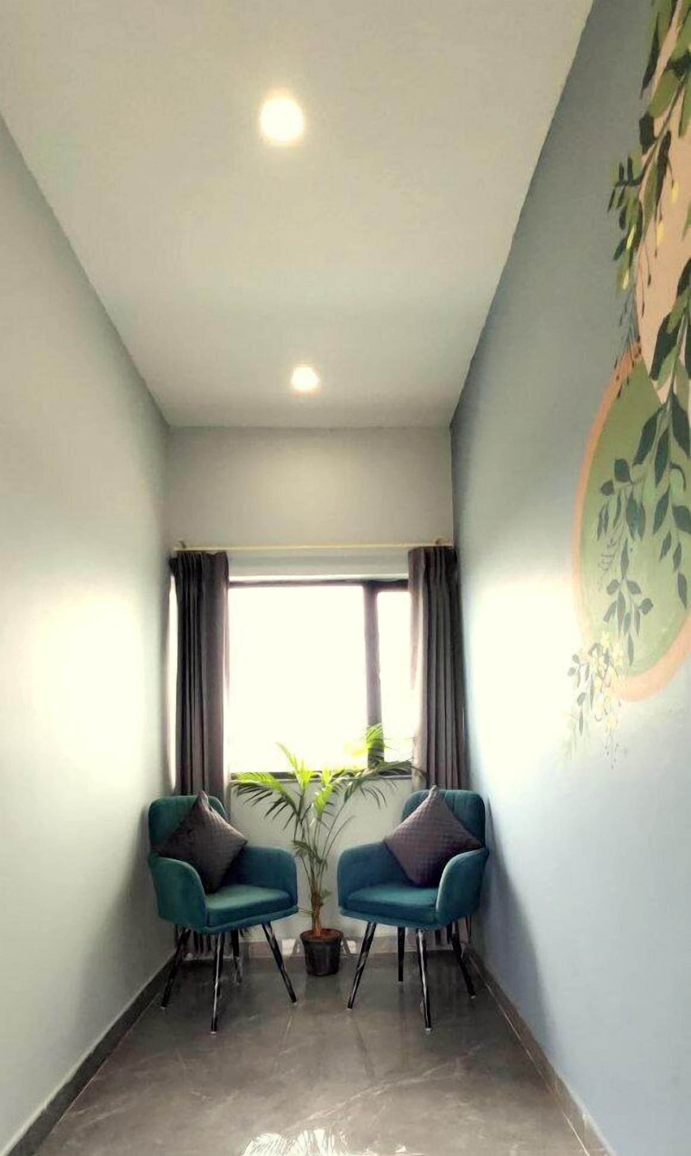 A room with a large window, two teal armchairs, a potted plant, and a wall with a leaf pattern.