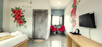 Una habitación de hotel con una cama, un escritorio, un televisor y dos sillas rojas.