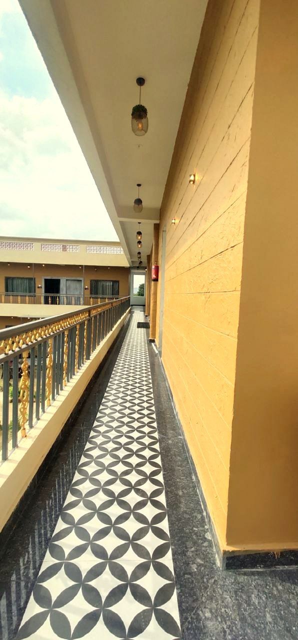 Un pasillo con suelo estampado, pared amarilla y un balcón con barandilla.
