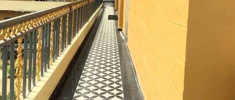 Un pasillo con suelo estampado, pared amarilla y un balcón con barandilla.