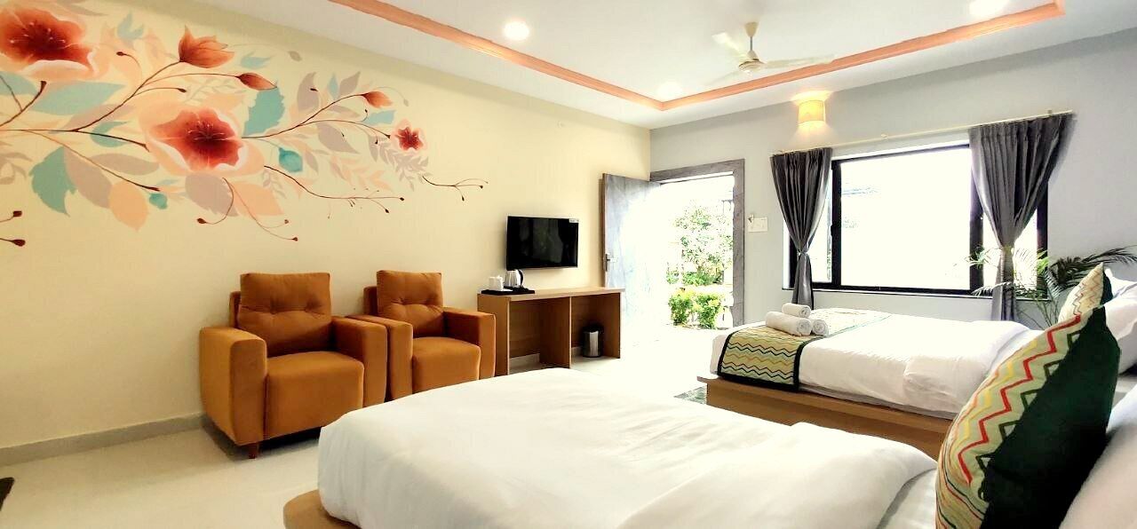 Habitación de hotel con una cama grande, dos sillones, televisión y ventana con cortinas.