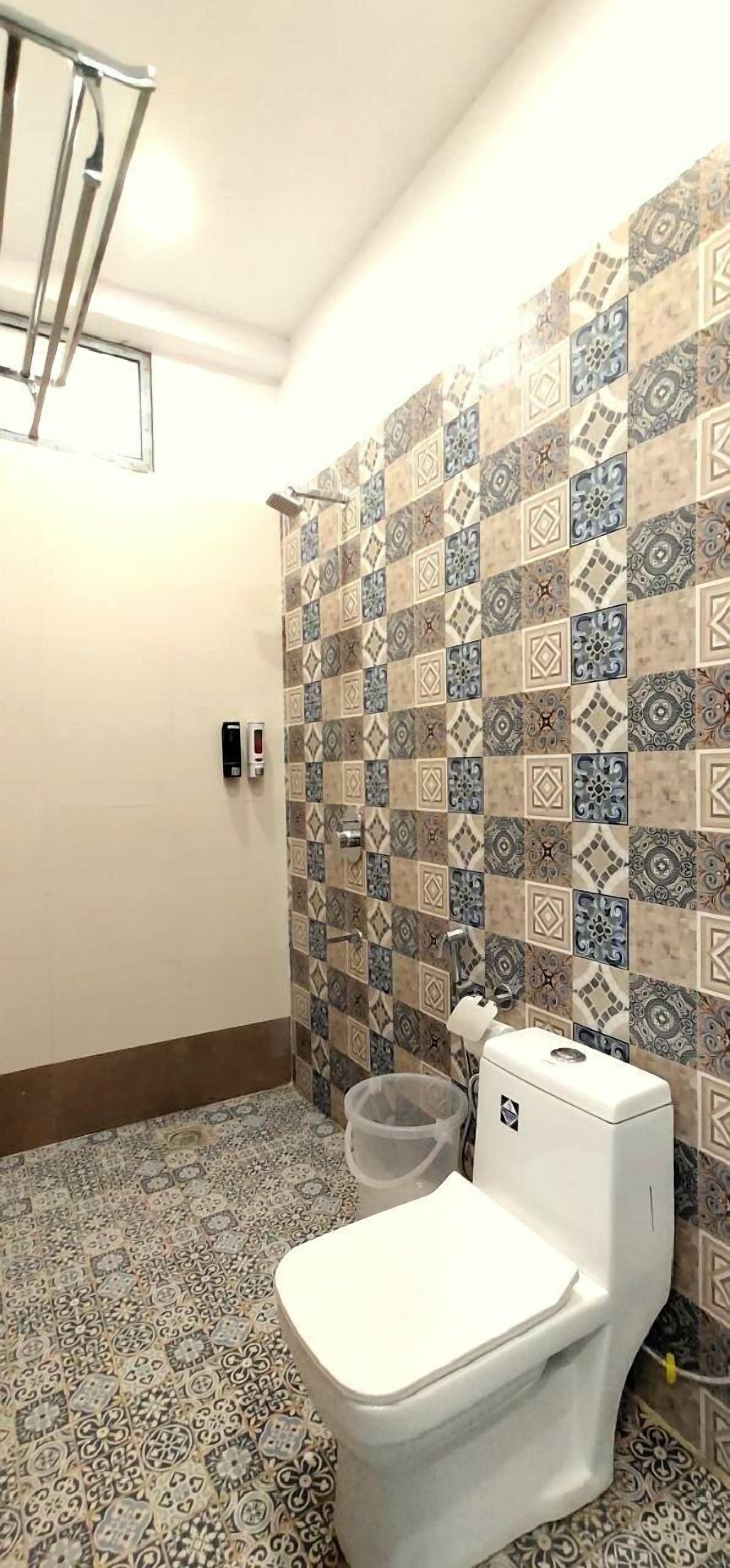 Un baño con baldosas estampadas, inodoro, un cubo de basura y un perchero para toallas.