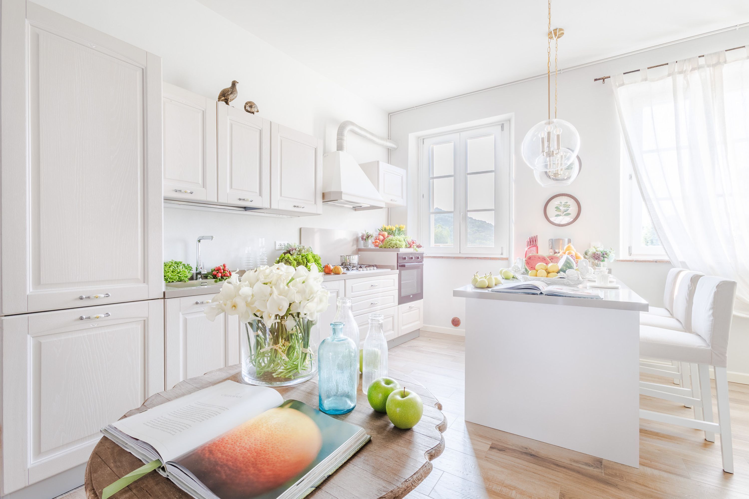 A modern kitchen with white cabinetry, a central island with seating, and a view of the outdoors.