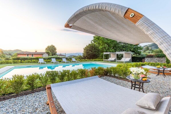 Ein Poolbereich mit Liegestühlen, einer überdachten Sitzgelegenheit und Blick auf die umliegende Landschaft.