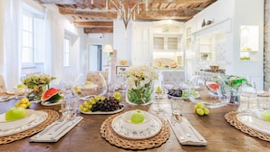 A dining table set with plates, glasses, and fruits, in a room with exposed wooden beams and white walls. - Villa Brera in Vorno (Capannori)