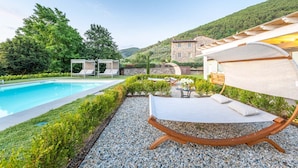 A poolside area with a lounge chair, a pergola, and a stone building in the background. - Villa Brera in Vorno (Capannori)