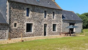 A stone building with multiple windows and a door, a small outdoor seating area with a table and chairs, and a grassy lawn. - Charming cottage in the countryside (6 bedrooms) (Saint-Clet)
