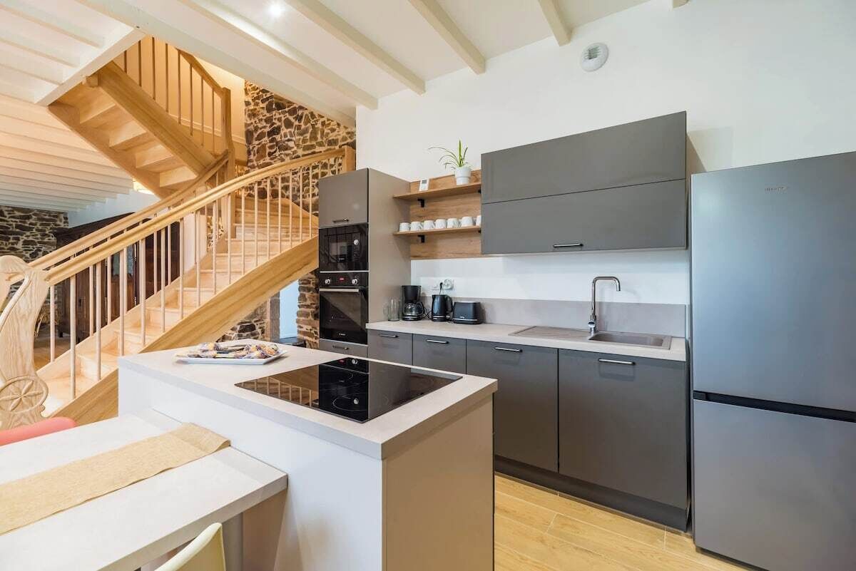 Eine moderne Küche mit Kochinsel, integrierten Geräten und einer Holztreppe.