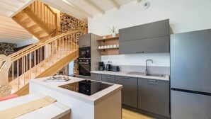 A modern kitchen with a central island, built-in appliances, and a wooden staircase. - Charming cottage in the countryside (6 bedrooms) (Saint-Clet)