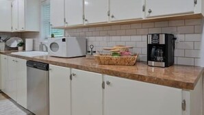 Una cocina con armarios blancos, microondas, cafetera y una cesta de objetos sobre la encimera.