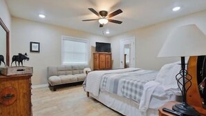 Un dormitorio con cama, cómoda de madera, sofá, ventilador de techo y lámpara.