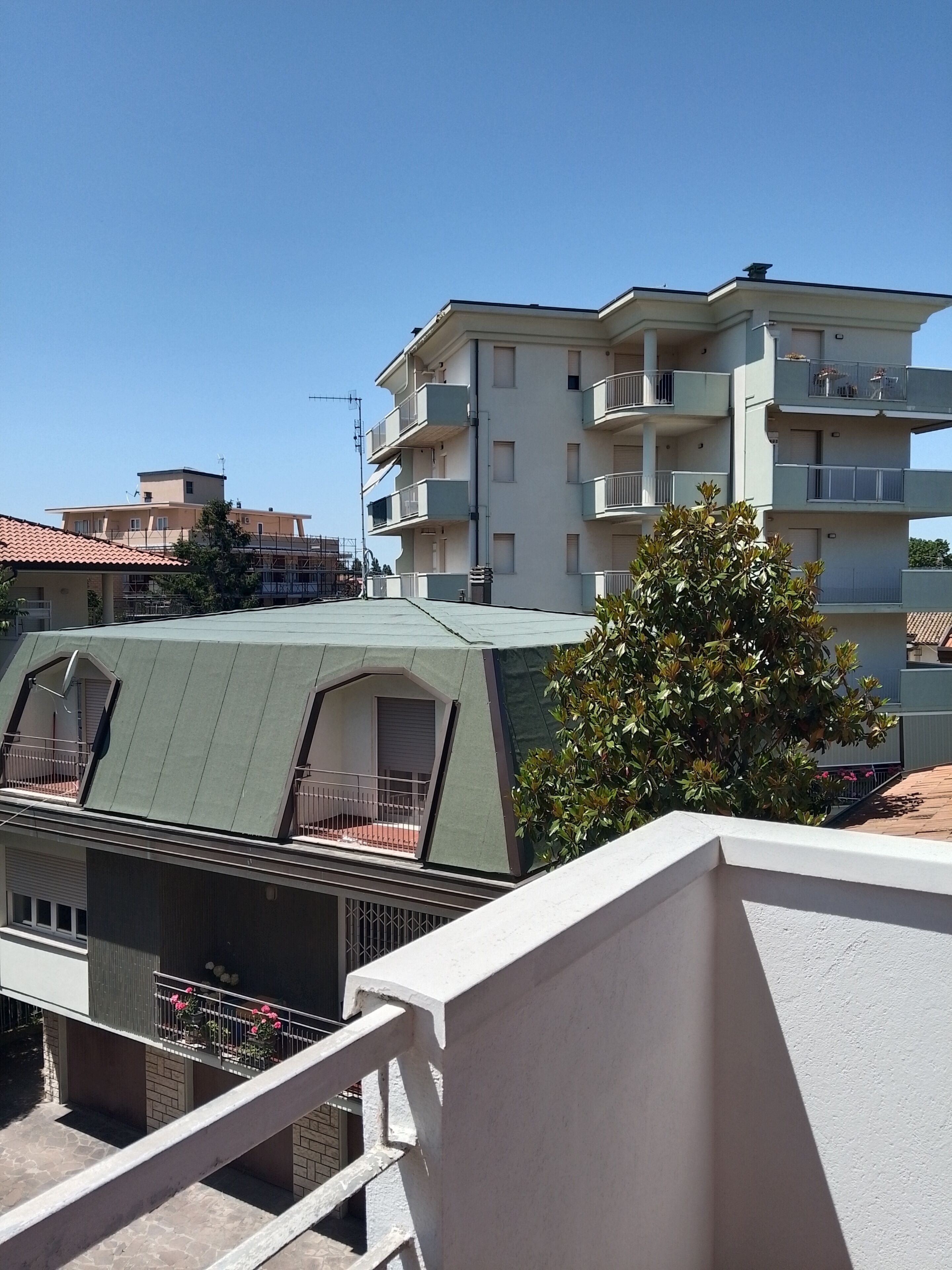 Un immeuble résidentiel à plusieurs étages, doté de balcons, d’un toit végétalisé et d’un arbre au premier plan.