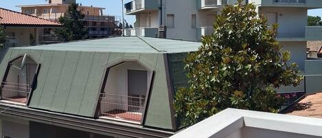 Un immeuble résidentiel à plusieurs étages, doté de balcons, d’un toit végétalisé et d’un arbre au premier plan.