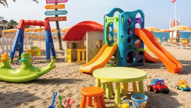 Ein Strandspielplatz mit Rutschen, Schaukeln und einem kleinen Gebäude.