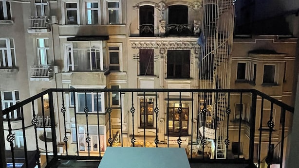 A balcony with a table and two chairs, overlooking a row of buildings with balconies and windows. - Taksim İnci Apart (İstanbul)