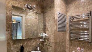 A modern bathroom with a marble wall, a white sink, a mirror, a towel rack, and a toilet. - Taksim İnci Apart (İstanbul)