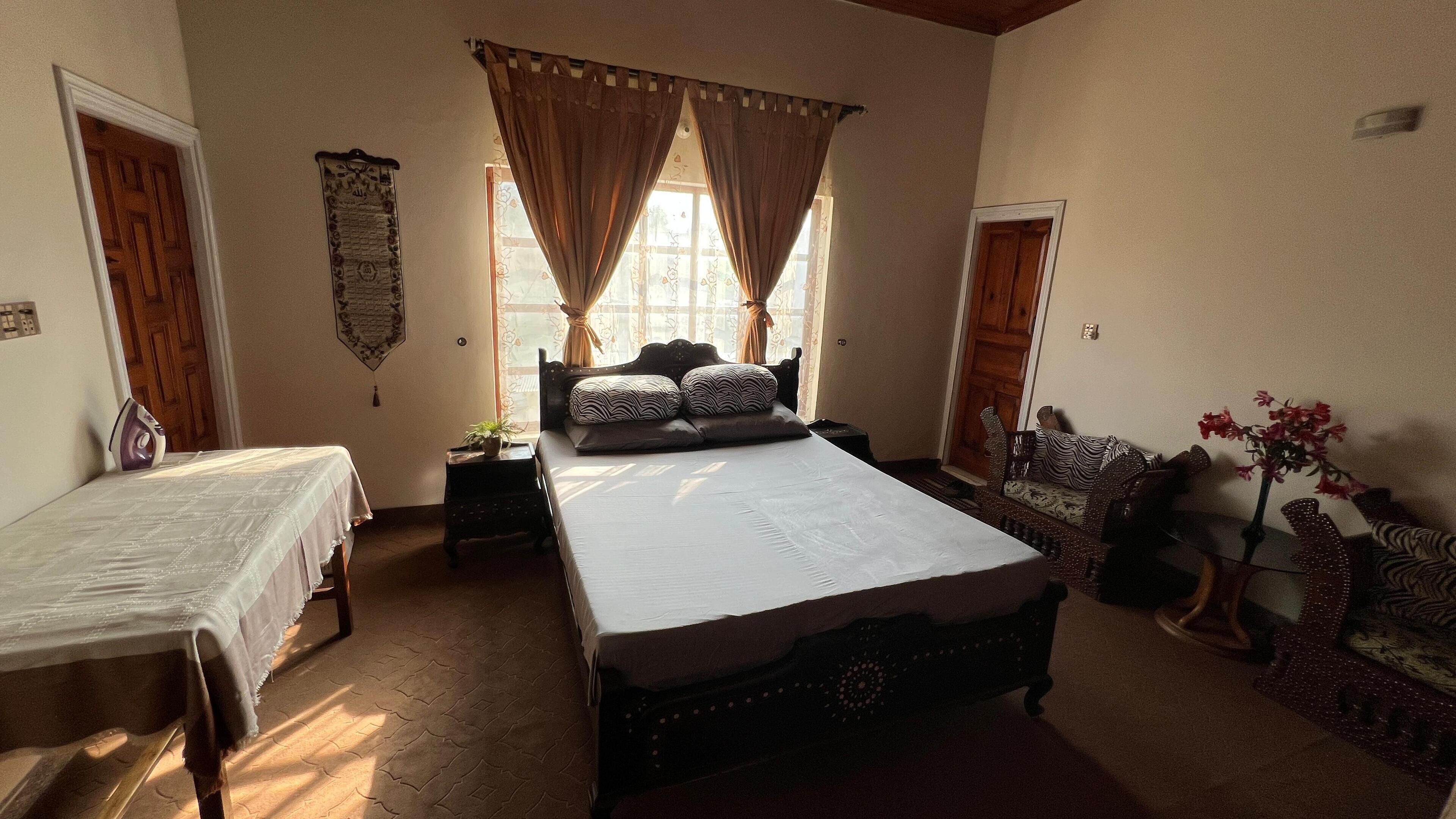 A bedroom with two single beds, a large bed with patterned pillows, a small table with a plant, and a decorative mirror.