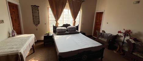 A bedroom with two single beds, a large bed with patterned pillows, a small table with a plant, and a decorative mirror.