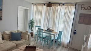 A cozy living room with a beige sofa, a small table with chairs, a wicker basket, and a potted plant. - Charming 1-bedroom, 1st Floor Condo in North Wildwood. 2 Blocks to Beach! (North Wildwood)