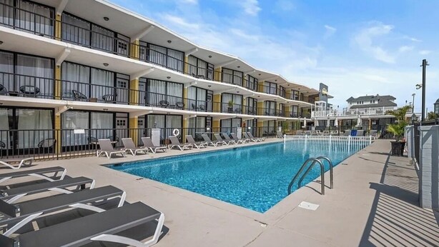 A hotel with a swimming pool, multiple balconies, and sun loungers. - Charming 1-bedroom, 1st Floor Condo in North Wildwood. 2 Blocks to Beach! (North Wildwood)