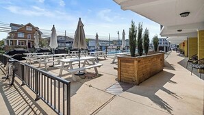 An outdoor patio area with picnic tables, umbrellas, and a wooden planter. - Charming 1-bedroom, 1st Floor Condo in North Wildwood. 2 Blocks to Beach! (North Wildwood)