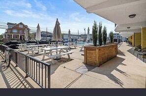 Ein Außenbereich mit einer Terrasse, Picknicktischen, Sonnenschirmen und einem hölzernen Blumenkasten.