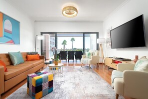 Uma sala de estar moderna com sofá, poltronas, mesa de centro, televisão e uma grande janela com vista.