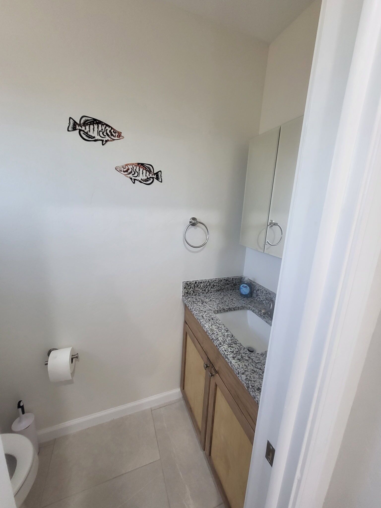 A bathroom with a toilet, sink, and mirror. There are two fish decals on the wall.