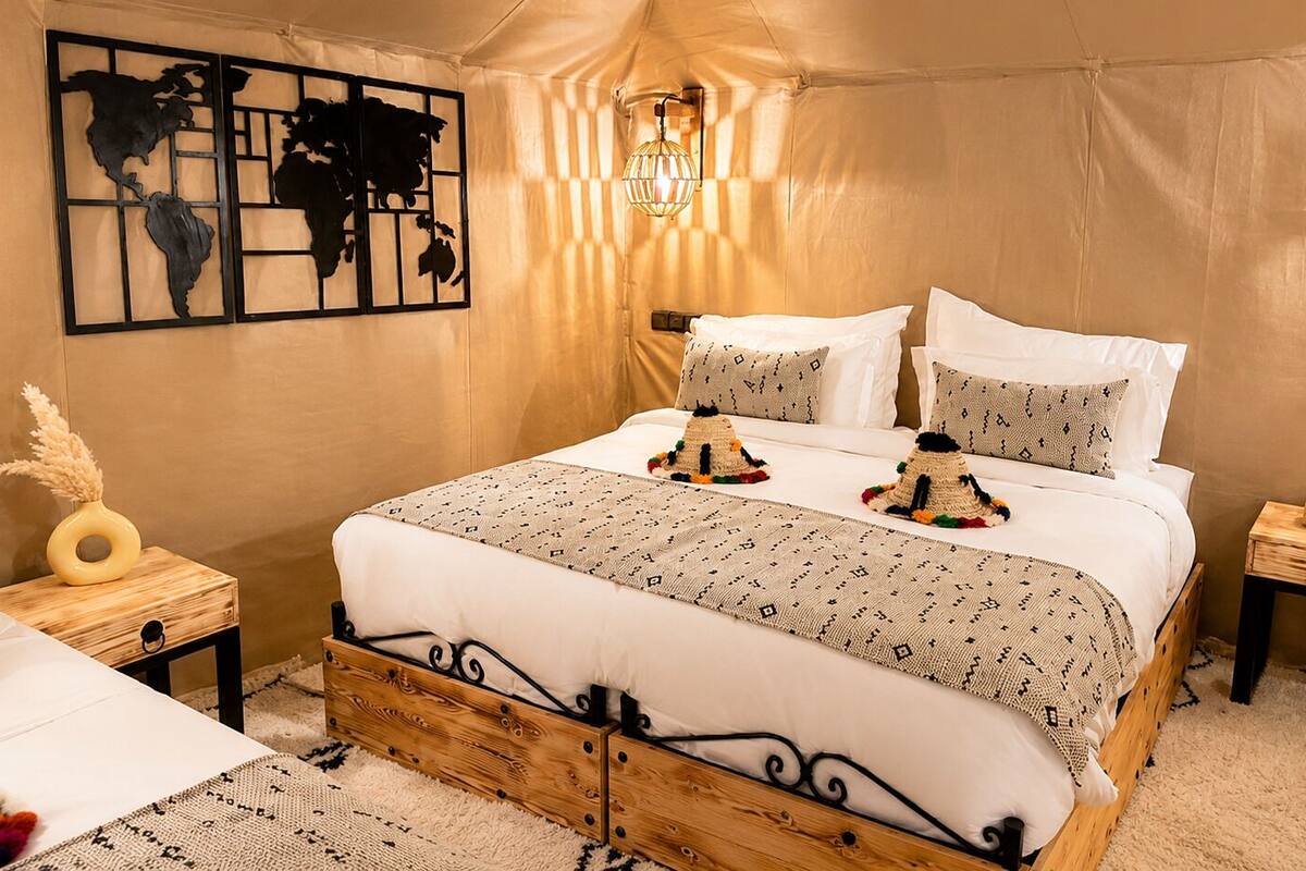 A tented room with a bed, a wall art piece, a lamp, and a small wooden nightstand.