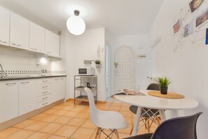 A modern kitchen with white cabinets, a dining table with chairs, a microwave, and a potted plant.