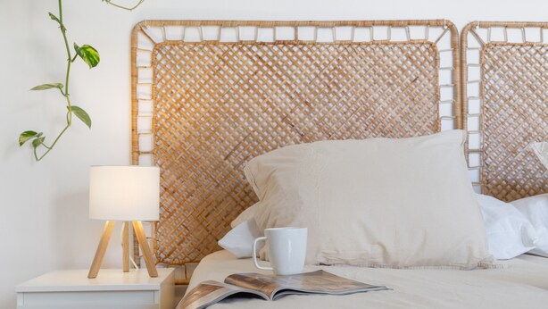 A bed with a woven headboard, a bedside lamp, a white mug, and a magazine on the bed.