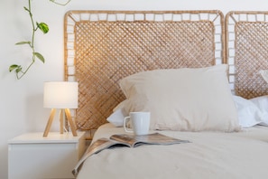 A bed with a woven headboard, a bedside lamp, a white mug, and a magazine on the bed. - Vacation 'Chill Life Corralejo Centre' with Balcony and Wi-Fi (Corralejo)