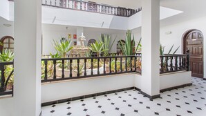 A multi-level interior with a tiled floor, a central fountain, and a balcony with a railing.
