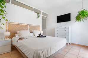 A bedroom with a bed, a TV, a dresser, and a hanging plant.