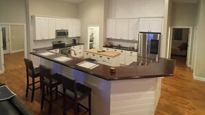 Een ruime keuken met een centraal eiland, witte kasten en roestvrijstalen apparatuur.