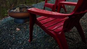Een rode Adirondack-stoel en een vuurkorf in een bebost gebied.