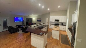 Een moderne keuken met witte kasten, een centraal eiland en een zithoek met een bank en televisie.